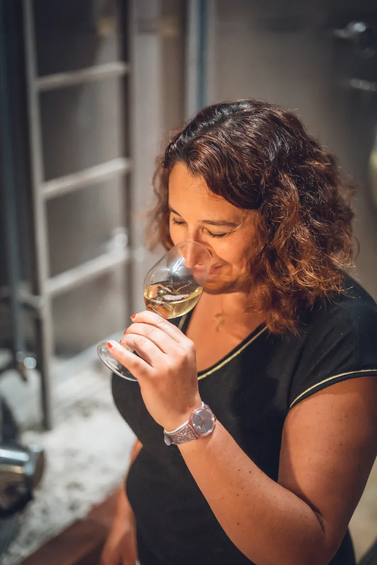A Wolfberger winemaker nosing a glass of white wine in the cellar.